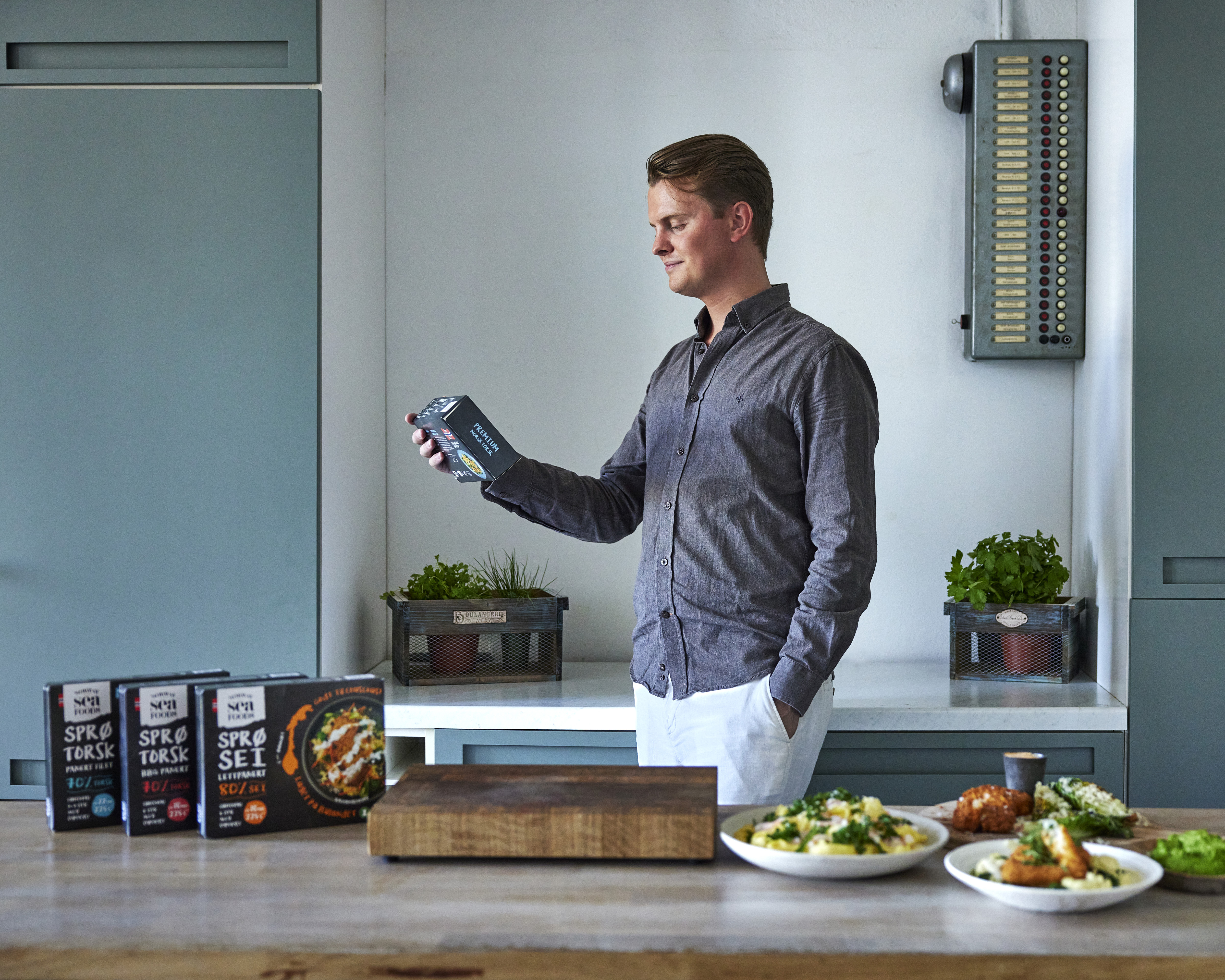 Simen leser på en forpakning, han er på et kjøkken. Foran han er Norway Seafoods produkter i forpakninger. 