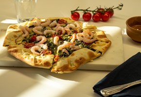 pizza sett fra siden med reker, spinat, chili, tomat. Bak er et vannglass og cherrytomater